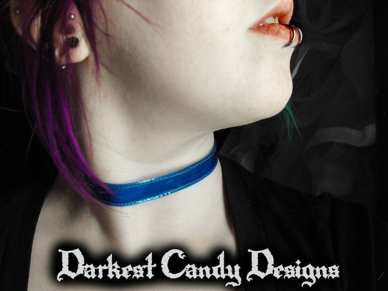 May include: A close-up of a blue velvet choker necklace. The choker is worn around the neck. The text "Darkest Candy Designs" is displayed in a gothic font at the bottom of the image.