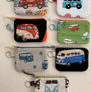 May include: Collection of small, rectangular coin purses featuring colorful illustrations of vintage camper vans. Each purse has a zipper closure, a key ring, and a fabric loop. The purses showcase various designs, including floral patterns and geometric shapes.