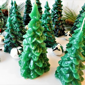 Puede incluir: Velas verdes con forma de árbol de Navidad con una superficie texturizada. Las velas están dispuestas con cascabeles plateados y ramitas de agujas de pino con bayas rojas. Una decoración festiva.