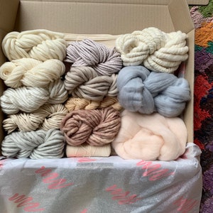 Puede incluir: Una caja llena de diferentes tonos de hilo y lana, incluyendo blanco, crema, rosa claro, marr&oacute;n claro y gris. El hilo est&aacute; organizado de forma ordenada y preparada para proyectos de manualidades.