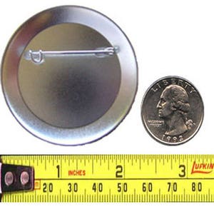 Pu&ograve; includere: Un bottone argentato con uno spillo sul retro. Il bottone ha un diametro di 2,5 cm. Una moneta da 25 centesimi di dollaro americano &egrave; mostrata per il confronto delle dimensioni.