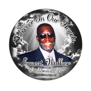 May include: A black and white memorial photo with a cloud background. The photo features a man wearing a suit and sunglasses. The text "Forever In Our Hearts" is written in a circle around the photo. The text "Ernest Walker" and "1/10/55 - 4/22/21" is written below the photo.