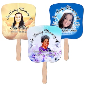 Pode incluir: Três leques comemorativos com cabos de madeira. Cada leque apresenta uma foto e o texto "In Loving Memory of" com um nome e datas. Os leques têm diferentes cores de fundo, incluindo azul, amarelo e branco.