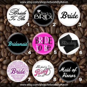 May include: A collection of nine round bridal-themed buttons. The buttons feature phrases like "Bride To Be," "Bridesmaid," and "Maid of Honor." Colors include black, white, pink, and purple. Some buttons have decorative elements like a ring or floral patterns.