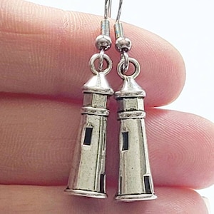 May include: Silver lighthouse earrings with a simple design. The earrings are on a silver hook.