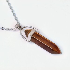 May include: A silver chain necklace with a brown tiger's eye crystal pendant. The pendant is shaped like a point and has a silver setting.
