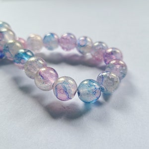 May include: A strand of iridescent glass beads with blue, pink, and white swirls. The beads are round and have a translucent appearance.