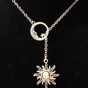 May include: A silver necklace with a crescent moon charm and a dangling sun charm. The moon charm has a star inside it.