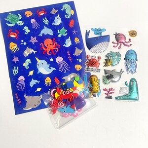 May include: A collection of ocean-themed stickers including a large blue sheet with various sea creatures, a clear sheet featuring 3D puffy stickers with text like "never stop" and "you can do it," and a small bag of colorful foam sea animal shapes.