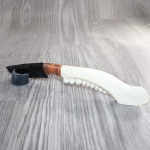 May include: A knife with a sharp, black, flaked stone blade attached to a curved, off-white bone handle featuring a row of visible teeth along the underside. The blade is secured to the handle with brown binding material near the base.