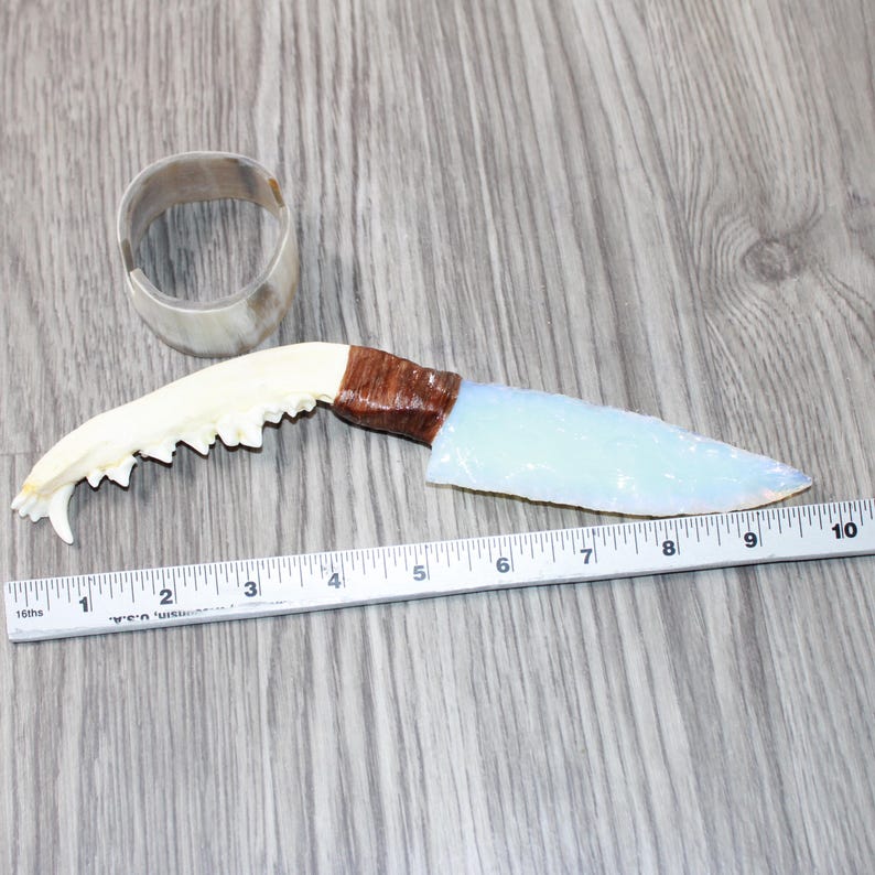 May include: A handmade knife with a light blue blade and a brown handle, next to a white ruler. The blade is approximately 5 inches long. A white bracelet is also in the image.