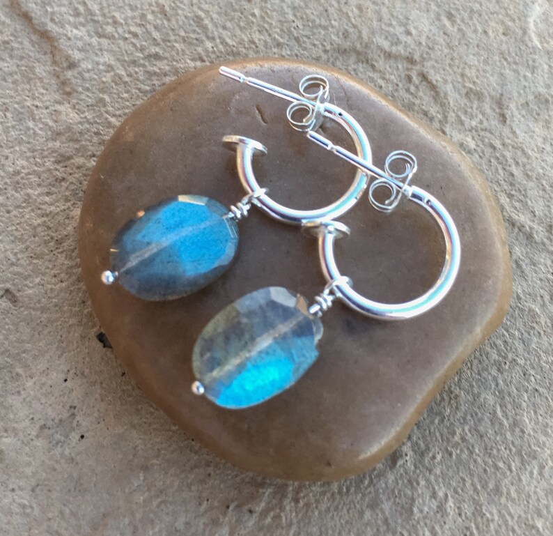 May include: Silver hoop earrings with a dangling oval-shaped blue labradorite gemstone.
