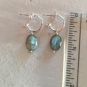 May include: Silver hoop earrings with a dangling oval labradorite gemstone. The earrings are approximately 1 inch long.