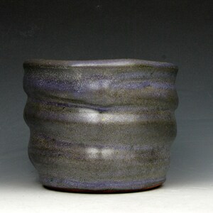 Può includere: Una tazza in ceramica fatta a mano con un esterno strutturato e ondulato. La tazza presenta una combinazione di colori grigio scuro e blu, con bande orizzontali di colore. Il bordo è leggermente irregolare, aggiungendo fascino rustico alla ceramica.