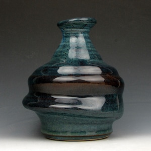 May include: A handcrafted ceramic vase with a unique, organic shape. The vase features a blend of teal, brown, and dark blue hues, with a glossy finish. The design includes a flared top and a bulbous body, showcasing the artist's skill.
