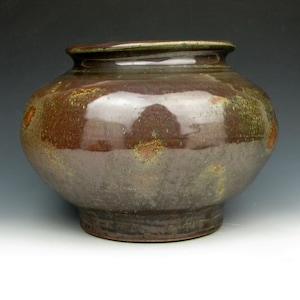 May include: A handcrafted ceramic vase with a rounded body and a slightly flared rim. The vase features a rich, earthy color palette of brown, rust, and olive green, with a glossy finish. The base is a darker shade of brown.