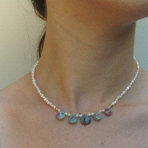 May include: A delicate pearl necklace with five green and pink gemstone pendants. The necklace is worn by a model.