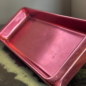 May include: A rectangular, rose-gold coloured metal tray with a smooth, slightly reflective surface. The tray has a slightly rounded edge.