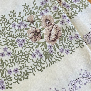 May include: A white tablecloth with a floral pattern. The pattern features green leaves, purple flowers, and brown flowers. The tablecloth has a paisley border.