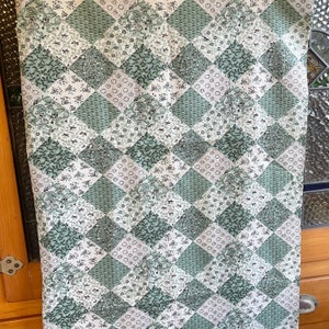 May include: A green and white fabric with a diamond pattern. The fabric is made of a patchwork of different floral prints.