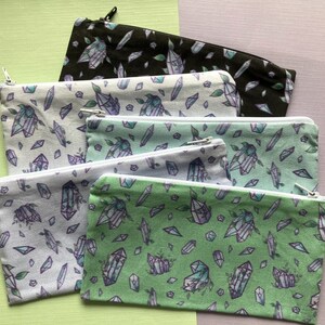 Könnte beinhalten: Fünf Reißverschlusstaschen mit Kristallmuster. Die Taschen sind in Grün-, Weiß- und Schwarztönen gehalten.