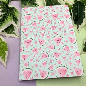 Puede incluir: Una libreta azul claro con un patrón repetido de rodajas de sandía rosadas.