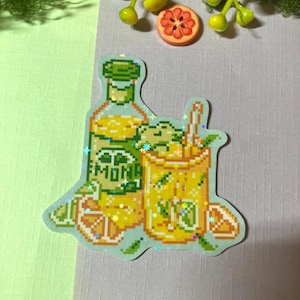 Könnte beinhalten: Ein holografischer Aufkleber mit Pixel-Art-Motiv einer Glasflasche und eines Glases gefüllt mit gelber Limonade, garniert mit grünen Limettenscheiben und Minzblättern. Das Flaschenetikett zeigt den Text LEMONADE in einem blockartigen Pixel-Schriftstil.