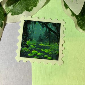 Könnte beinhalten: Eine grüne und blaue Illustration einer Sumpflandschaft mit leuchtenden Glühwürmchen und Seerosen. Die Illustration ist auf einem weißen Aufkleber mit einem gewellten Rand gedruckt.