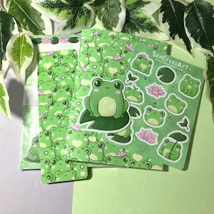 Könnte beinhalten: Briefpapier-Set mit grünem Frosch-Thema, einschließlich Aufklebern, Briefpapier und einer Karte. Die Frosch-Illustrationen sind in verschiedenen Grün- und Weißtönen gehalten. Die Karte trägt den Text "SenCrossArt".