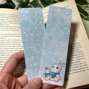 Könnte beinhalten: Zwei blaue Lesezeichen mit einem Schneeflockenmuster. Ein Lesezeichen zeigt einen Schneemann und ein Kaninchen mit einem blauen Schal. Das andere Lesezeichen hat ein Schneeflockenmuster.