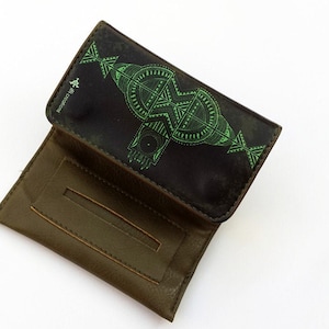 May include: A brown leather cigarette rolling case with a green geometric design. The case is open and the inside is lined with brown fabric.