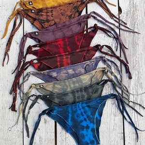 Pode incluir: Uma pilha de sete partes de baixo de biquíni tie-dye coloridas com laços ajustáveis. As partes de baixo são feitas de um tecido macio e sedoso e apresentam uma variedade de padrões tie-dye.