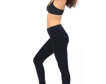 May include: A woman wearing black leggings and a black sports bra. She is standing with her arms raised above her head and her hair is pulled back.