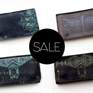 May include: Four leather wallets with unique designs. Each wallet is rectangular and features a different geometric or nature-inspired pattern in shades of green and blue. The word "SALE" is in a black circle.