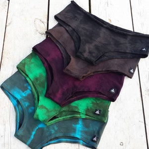 Könnte beinhalten: Ein Stapel aus fünf Paaren von Batik-Unterwäsche in verschiedenen Grüntönen, Blau- und Lilatönen. Die Unterwäsche ist aus einem weichen, bequemen Stoff gefertigt und hat eine lockere Passform.
