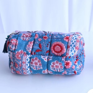 May include: A quilted cosmetic bag featuring a floral design in blue, pink, and red. The rectangular bag has a zip closure and a small tassel. The fabric is patterned with stylized flowers and leaves. The bag is approximately 20 cm long.