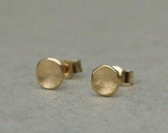 May include: A pair of small, round, gold earrings. The earrings have a textured, hammered finish.