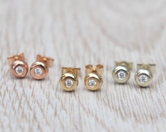 May include: Three pairs of small stud earrings with a single round diamond in the centre. The earrings are in three different metal finishes: rose gold, yellow gold, and white gold.