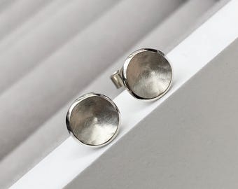 May include: A pair of silver stud earrings with a round, slightly domed shape. The earrings have a brushed finish.