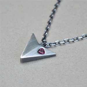 May include: Silver necklace with a triangular pendant featuring a small pink heart-shaped gemstone.