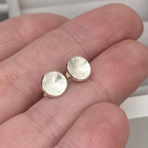 May include: A pair of silver hammered disc stud earrings. The earrings are round and have a textured surface.