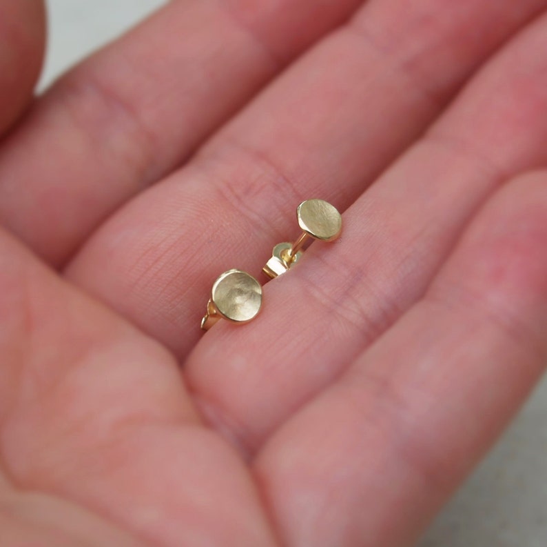 May include: A pair of small, round, gold earrings. The earrings are smooth and have a slightly textured surface.