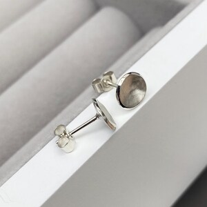 May include: A pair of silver stud earrings with a round, slightly concave design. The earrings are displayed in a white box.
