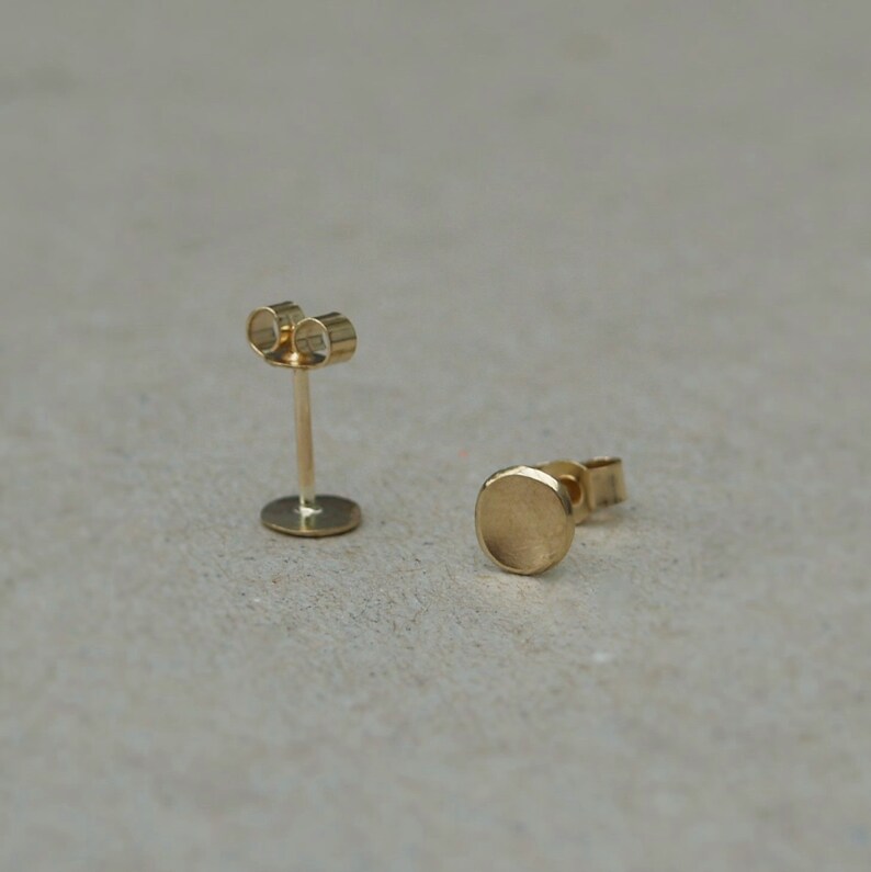 May include: A pair of gold stud earrings with a round, slightly textured design. The earrings are simple and minimalist.
