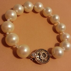 May include: A white pearl bracelet with a gold clasp. The clasp has a decorative design and a small clear rhinestone.
