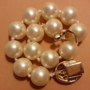 May include: A white pearl bracelet with a gold clasp. The clasp has the word "Mikimoto" engraved on it.