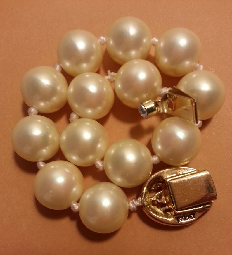 May include: A white pearl bracelet with a gold clasp. The clasp has the word "Mikimoto" engraved on it.