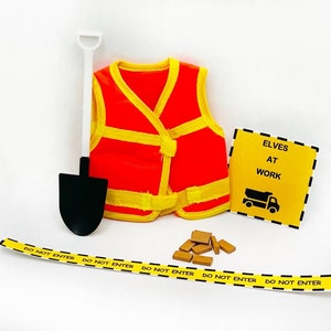 May include: A set of elf construction worker props, including a safety vest, a shovel, a sign that reads "Elves at Work", and a yellow and black caution tape that reads "Do Not Enter".