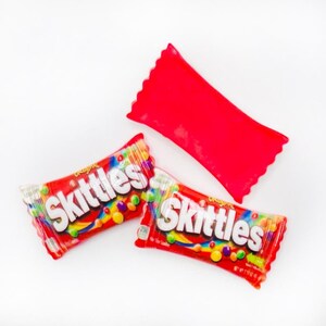 May include: Two red and white Skittles candy packages with the word "Skittles" printed in white on the front. The packages are on a white background.