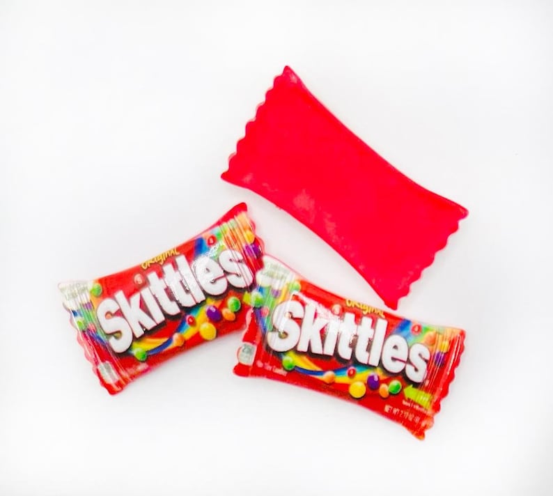 May include: Two red and white Skittles candy packages with the word "Skittles" printed in white on the front. The packages are on a white background.